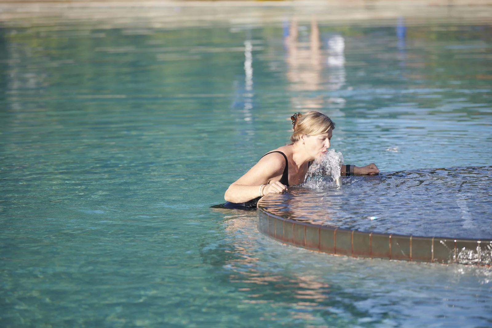 Frau trinkt das naturbelassene und stark kohlensäurehaltige Mineralwasser aus dem Trinkbrunnen im Aussenbecken im Mineralbad Berg.