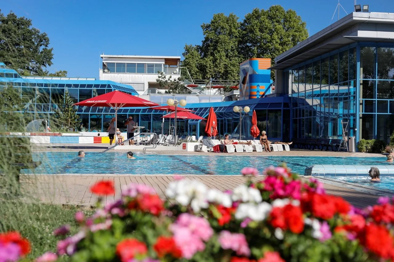 DAS LEUZE Aussenbereich mit Blick auf das Badgebaeude und die Schwimmbecken DAS LEUZE Aussenbereich mit Blick auf das Badgebaeude und die Schwimmbecken - eine Blumenrabatte im Vordergrund
