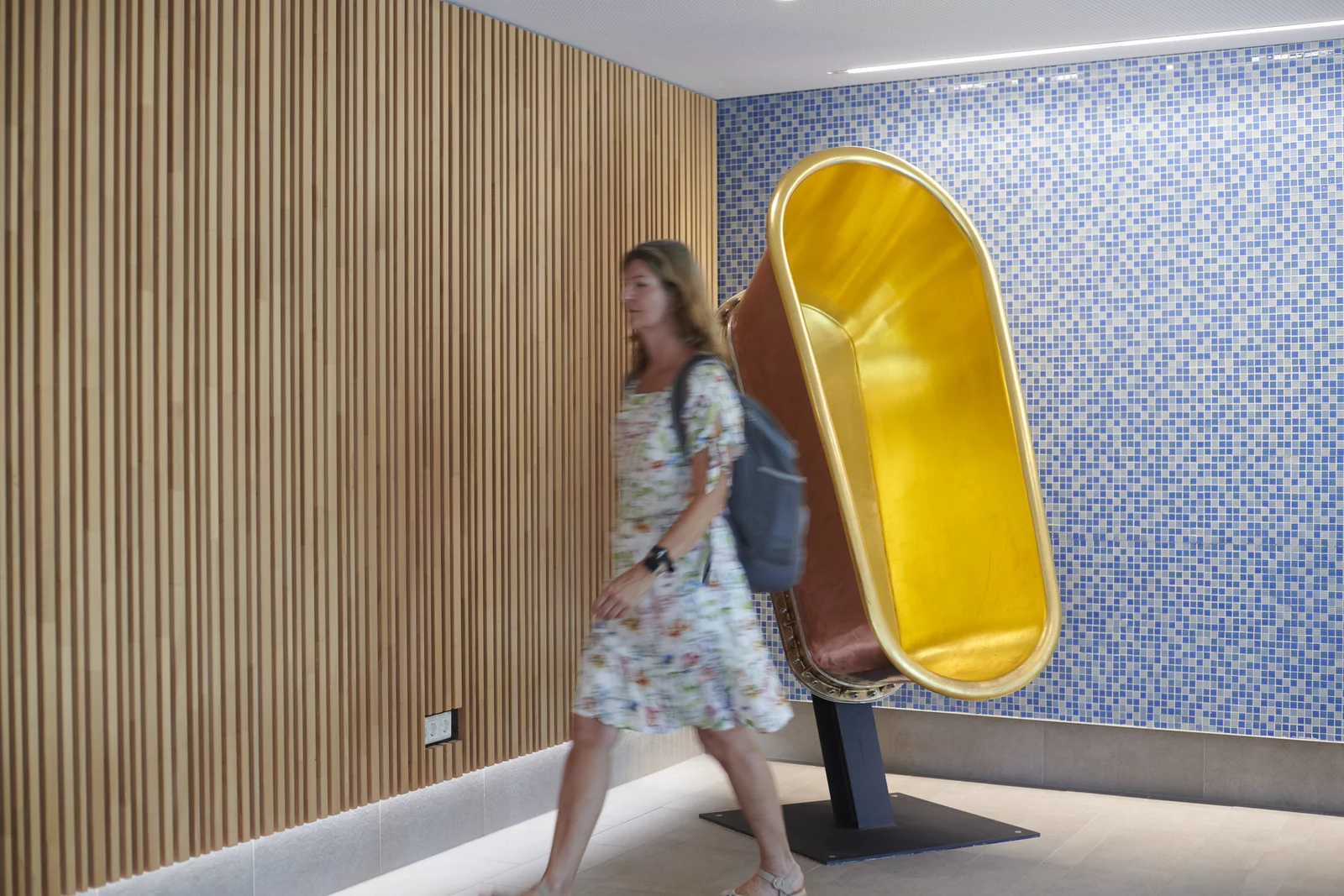 Eine Frau läuft vorbei an der goldenen Badewanne im 1. Stock des Foyes Mineralbad Berg.vorbei.