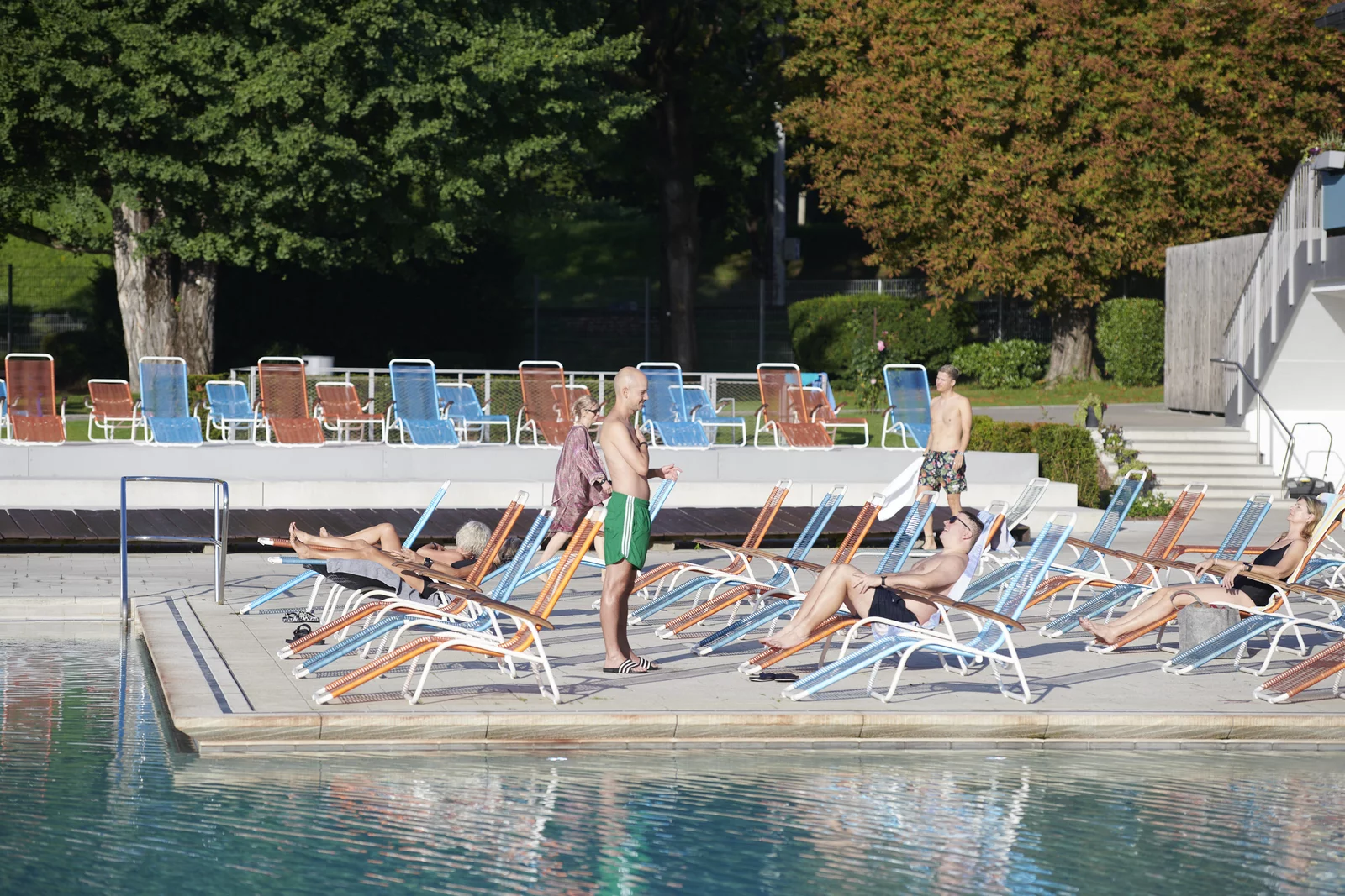 Eine Gruppe Badegäste auf den Liegen auf der Sonnenterrasse am Aussenbecken im Mineralbad Berg. Im Hintergrund ist eine grüne Parkanlage zu sehen.