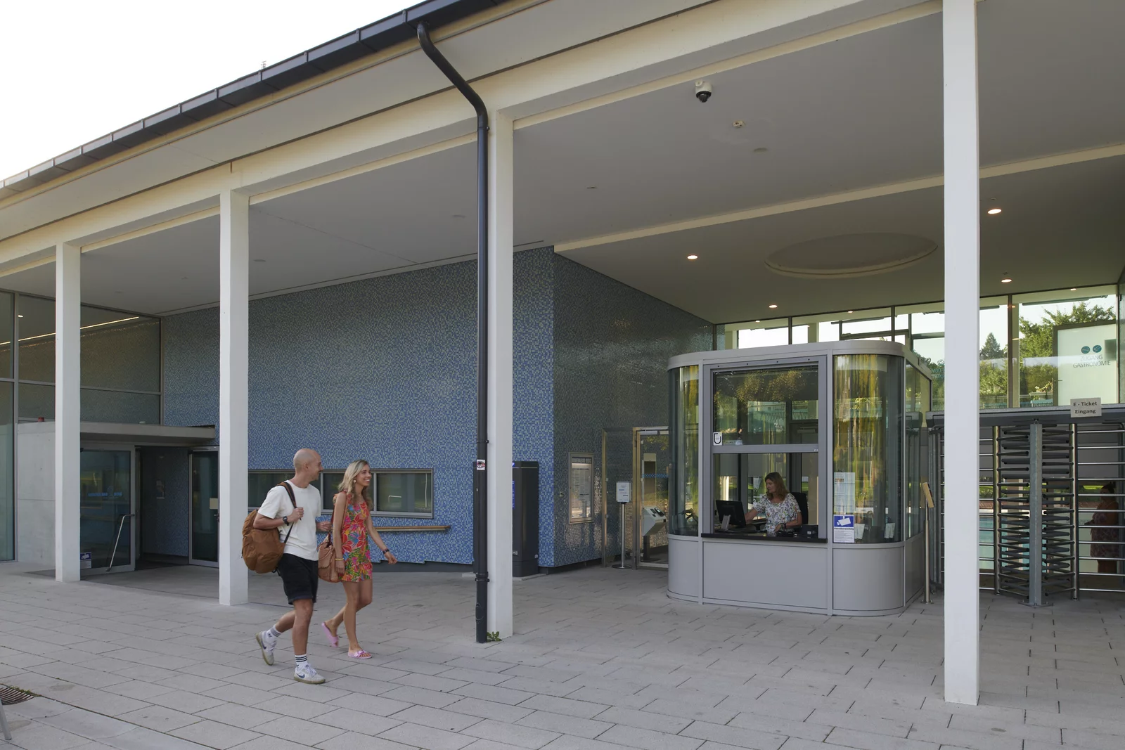 Ein jünges Paar läuft an der Badfassade entlang Richtung Kasse mit dem Drehkreuz-Eingang.