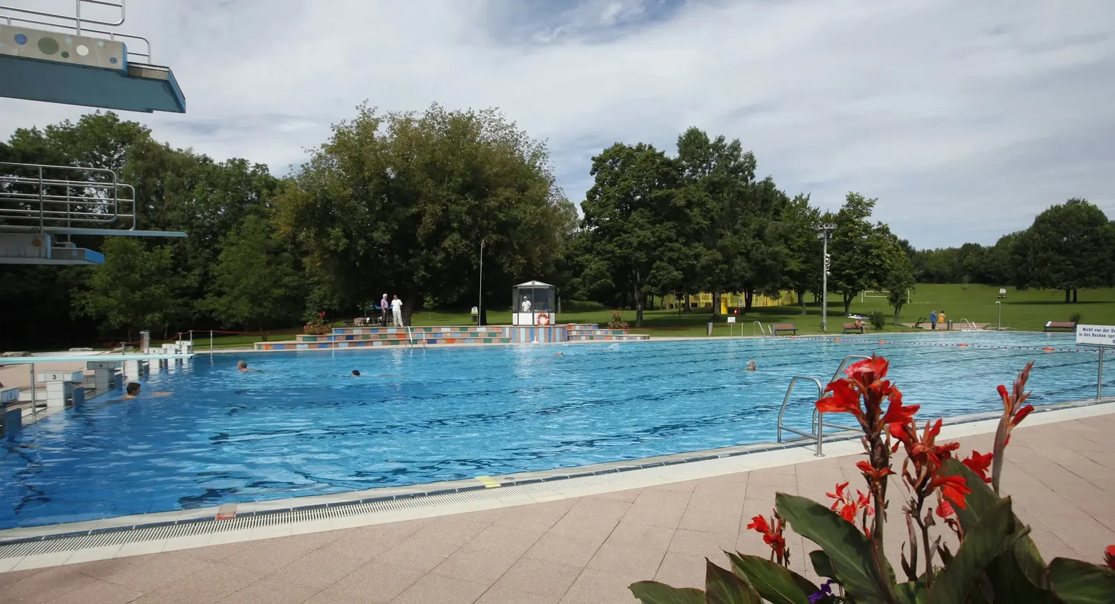 Außenansicht Mehrzweckbecken ohne Badegäste mit Sprungturm und einer Blumenrabatte im Freibad Möhringen.